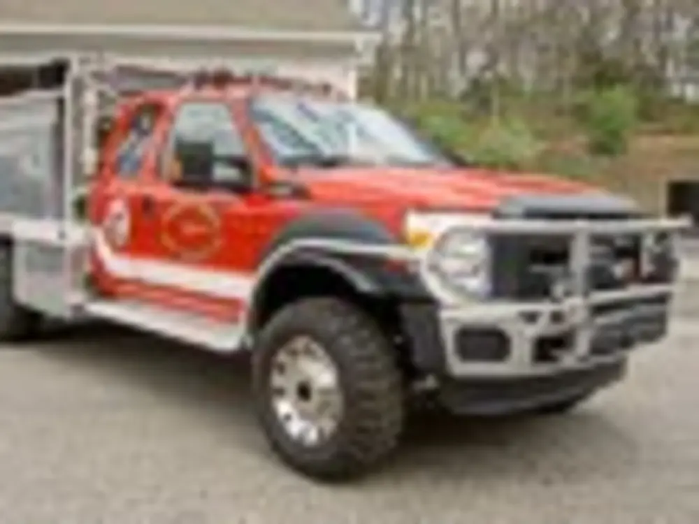 Exterior view of small fire truck showing cab, body compartments, and wheel/tire area.