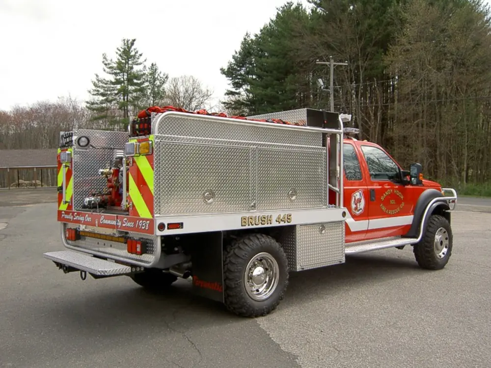 Exterior view of small fire truck showing cab, body compartments, and wheel/tire area.
