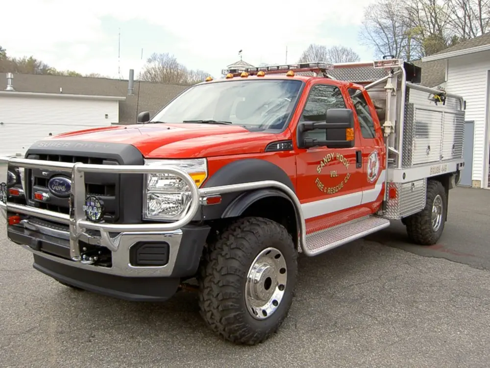 Exterior view of small fire truck showing cab, body compartments, and wheel/tire area.