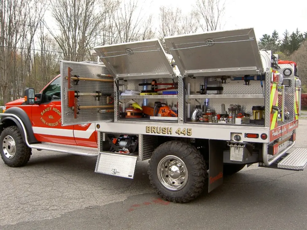Exterior view of small fire truck showing cab, body compartments, and wheel/tire area.