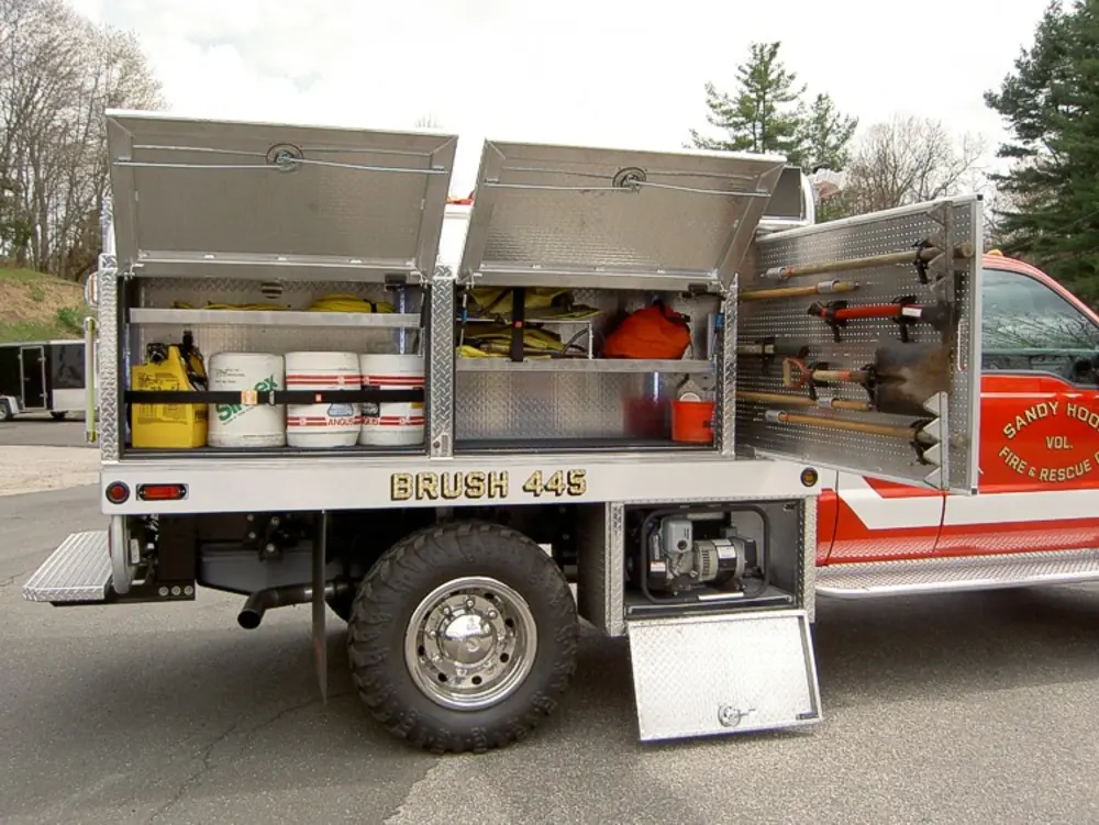 Exterior view of small fire truck showing cab, body compartments, and wheel/tire area.