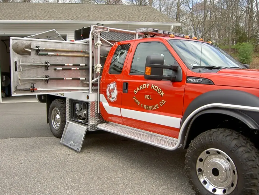 Exterior view of small fire truck showing cab, body compartments, and wheel/tire area.