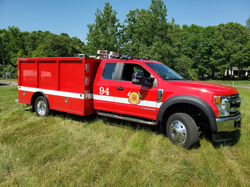 Exterior view of small fire truck showing cab, body compartments, and wheel/tire area.