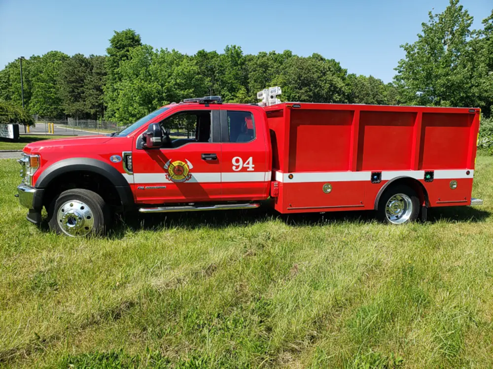 Exterior view of small fire truck showing cab, body compartments, and wheel/tire area.