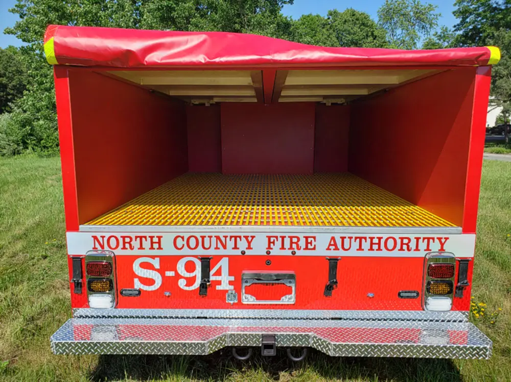 Exterior view of small fire truck showing cab, body compartments, and wheel/tire area.