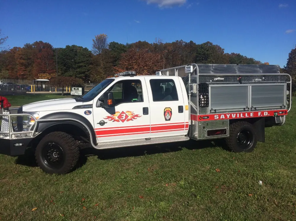 Exterior view of small fire truck showing cab, body compartments, and wheel/tire area.