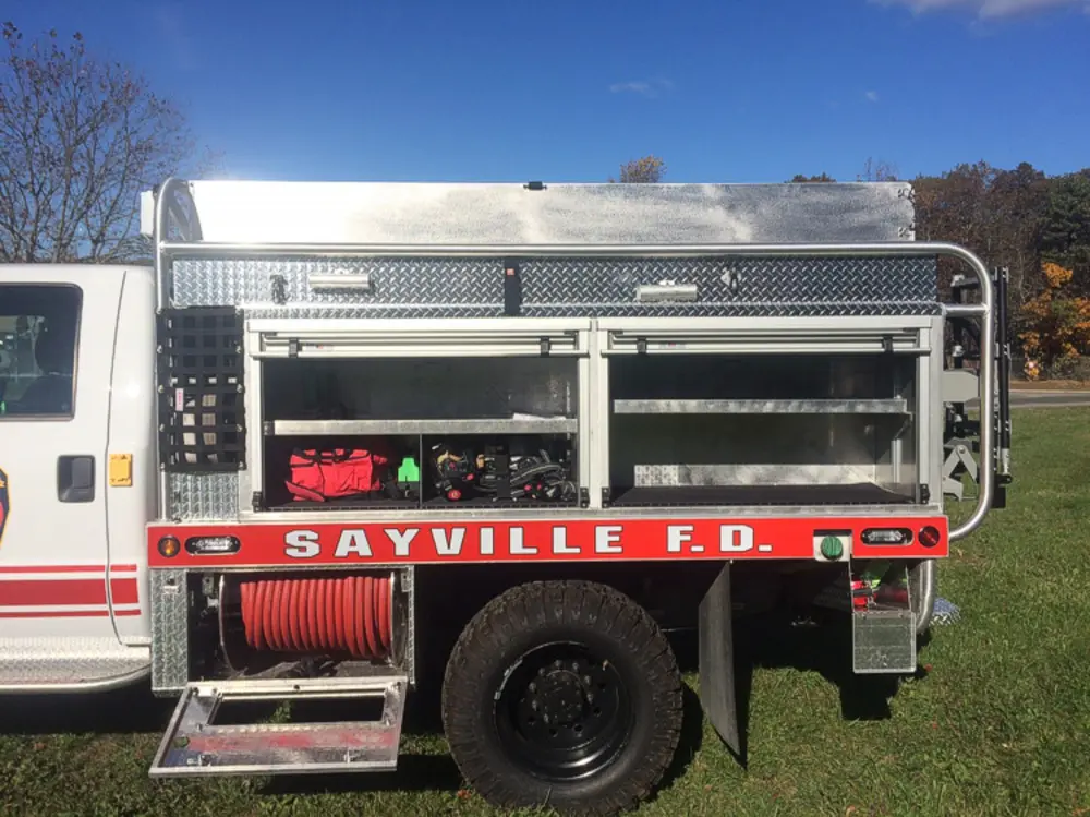 Exterior view of small fire truck showing cab, body compartments, and wheel/tire area.