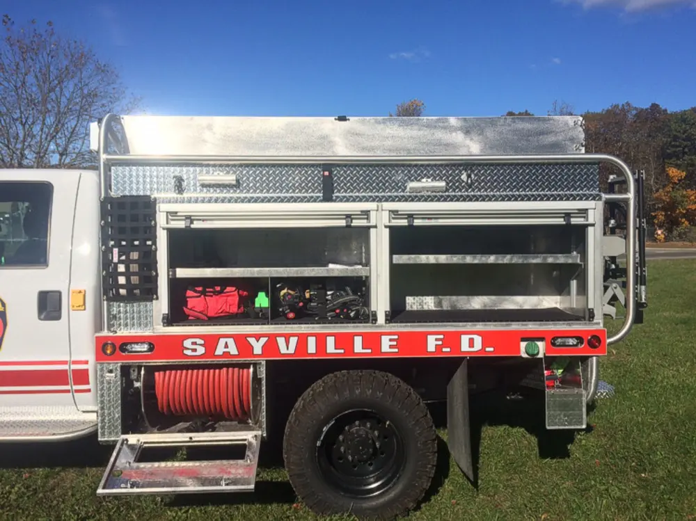 Exterior view of small fire truck showing cab, body compartments, and wheel/tire area.