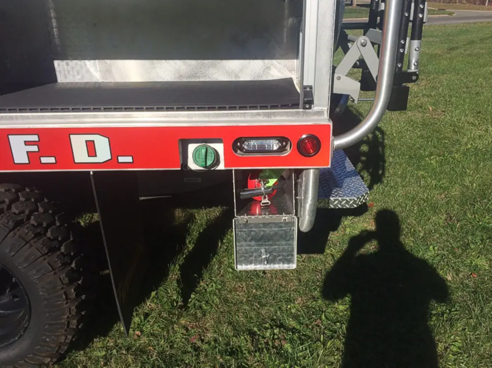 Exterior view of small fire truck showing cab, body compartments, and wheel/tire area.