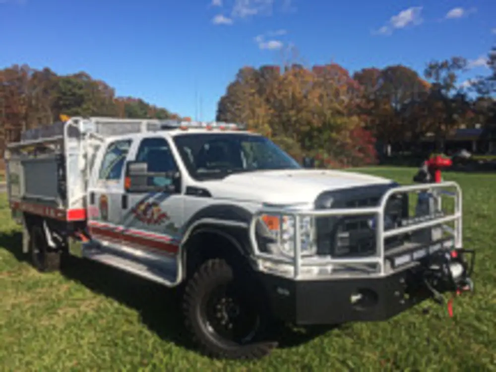 Exterior view of small fire truck showing cab, body compartments, and wheel/tire area.