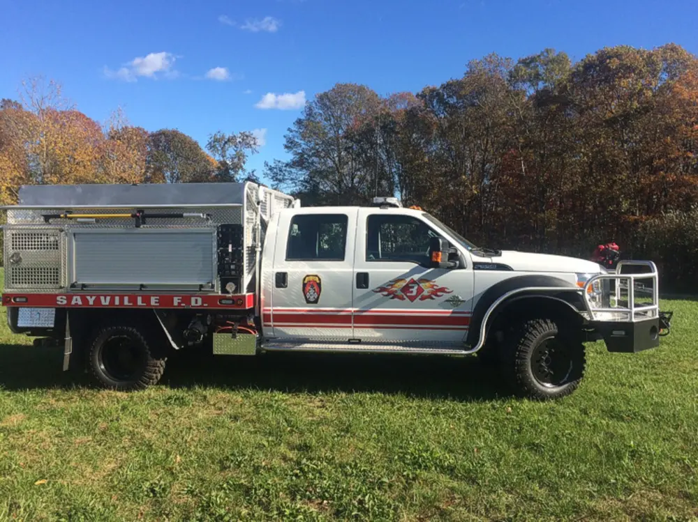 Exterior view of small fire truck showing cab, body compartments, and wheel/tire area.