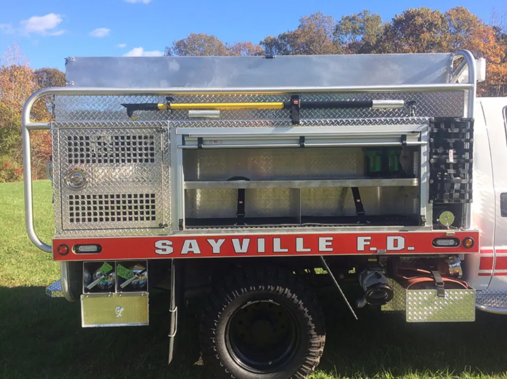 Exterior view of small fire truck showing cab, body compartments, and wheel/tire area.