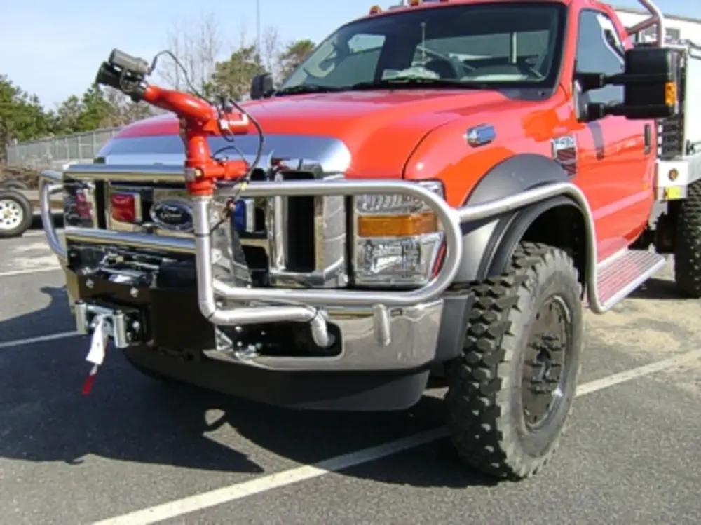Exterior view of small fire truck showing cab, body compartments, and wheel/tire area.
