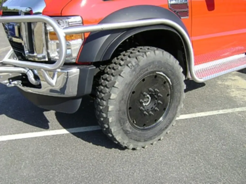 Exterior view of small fire truck showing cab, body compartments, and wheel/tire area.