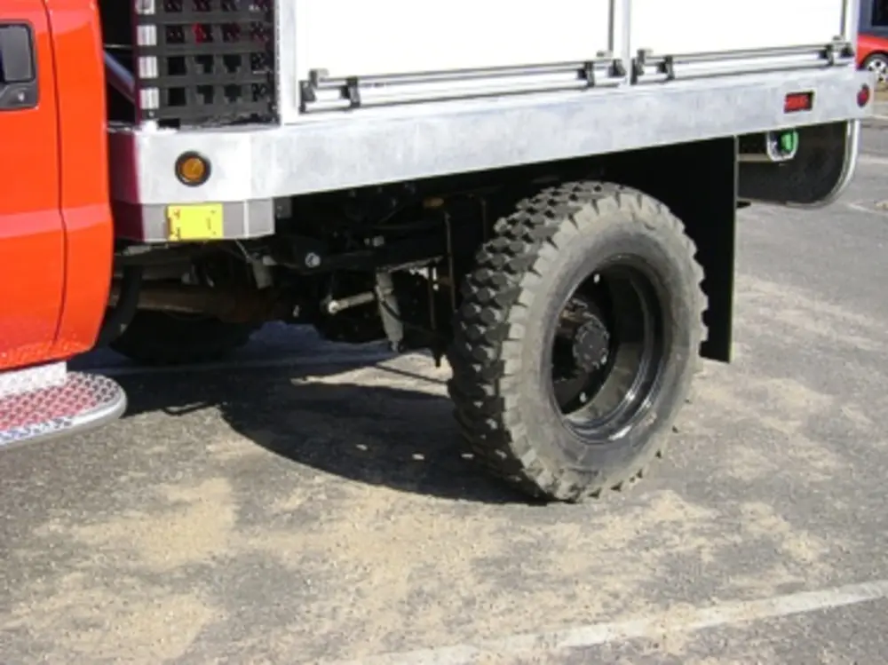 Exterior view of small fire truck showing cab, body compartments, and wheel/tire area.