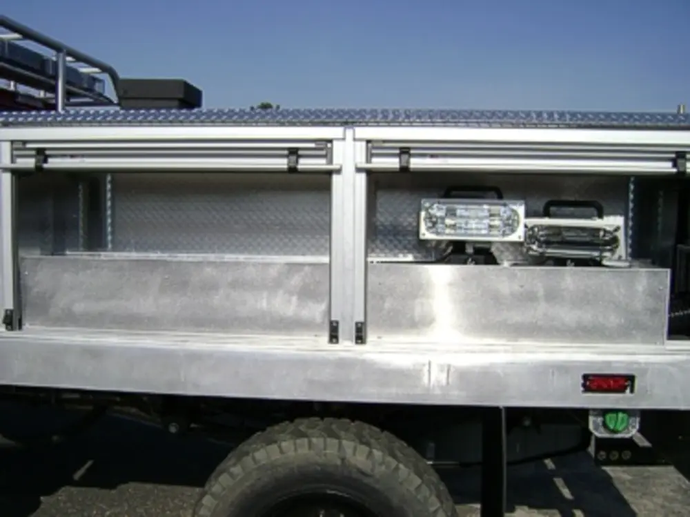 Exterior view of small fire truck showing cab, body compartments, and wheel/tire area.