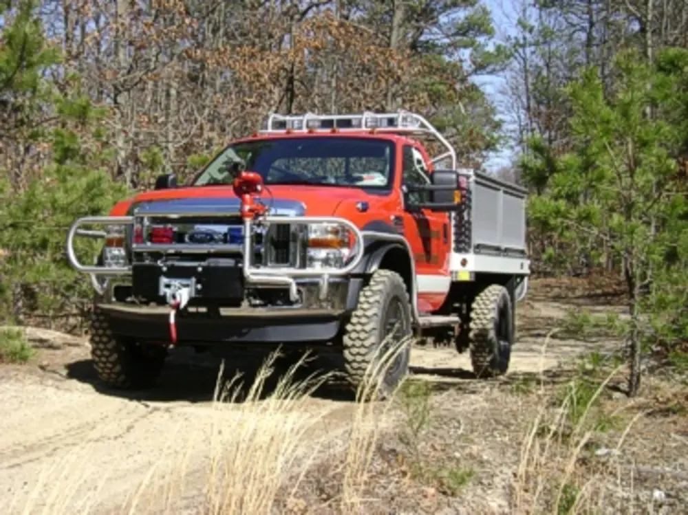 Exterior view of small fire truck showing cab, body compartments, and wheel/tire area.