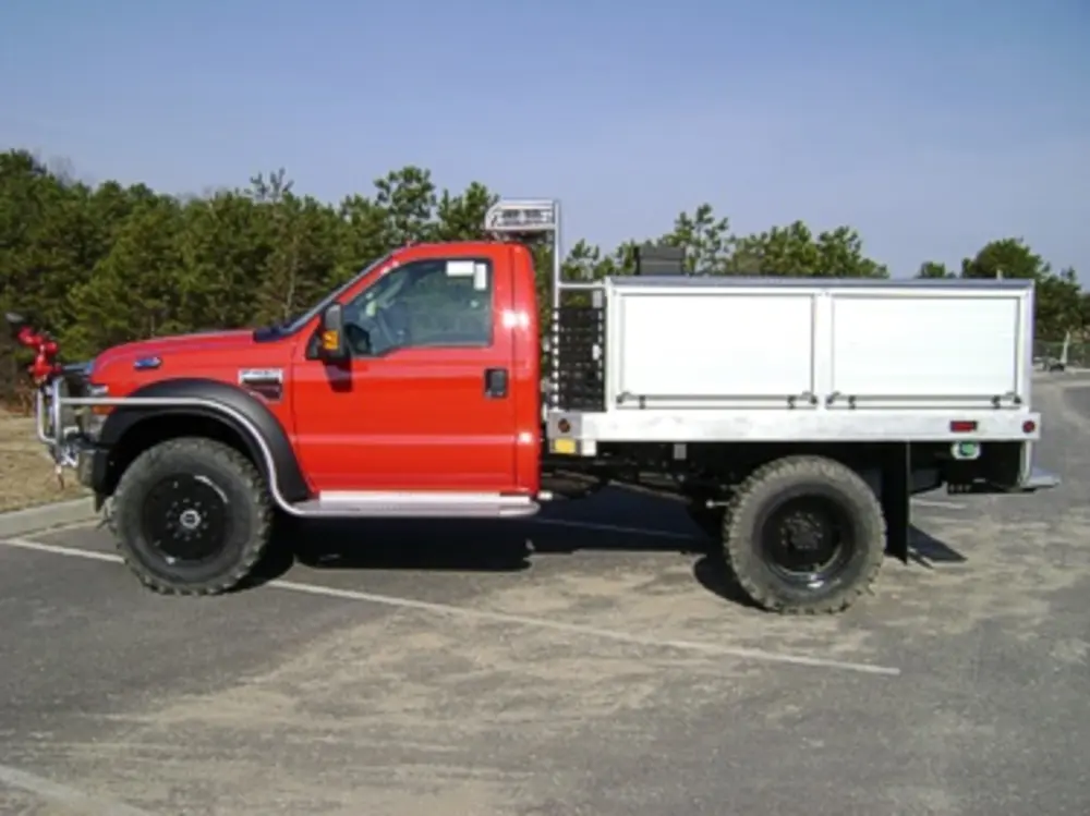 Exterior view of small fire truck showing cab, body compartments, and wheel/tire area.