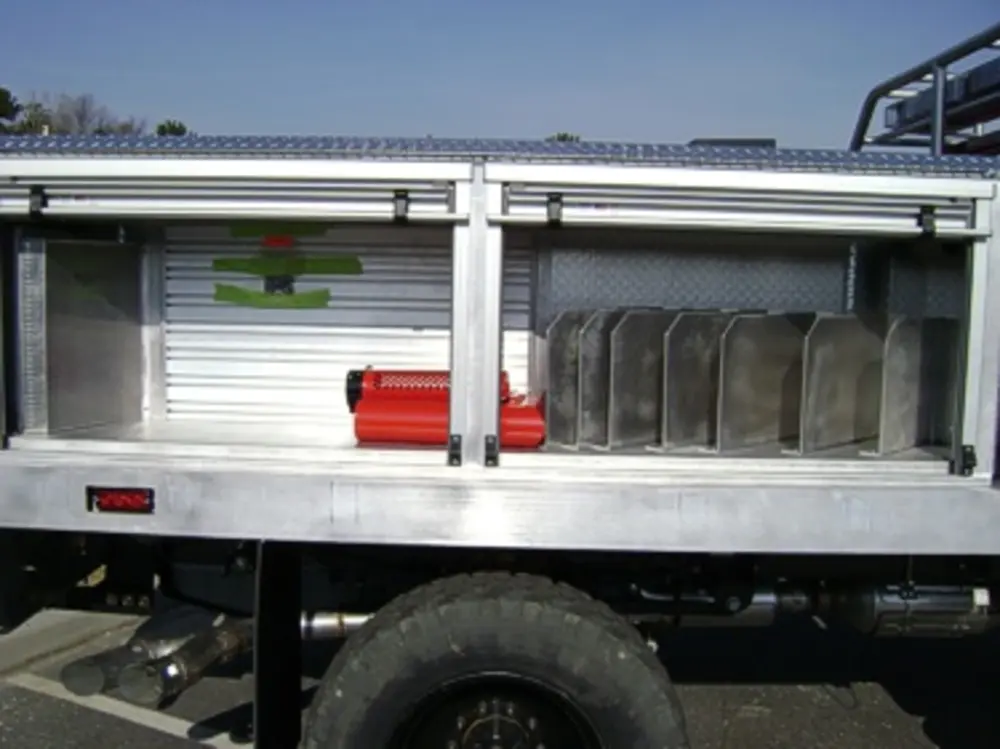 Exterior view of small fire truck showing cab, body compartments, and wheel/tire area.