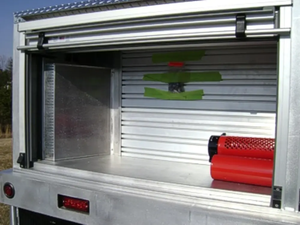 Exterior view of small fire truck showing cab, body compartments, and wheel/tire area.