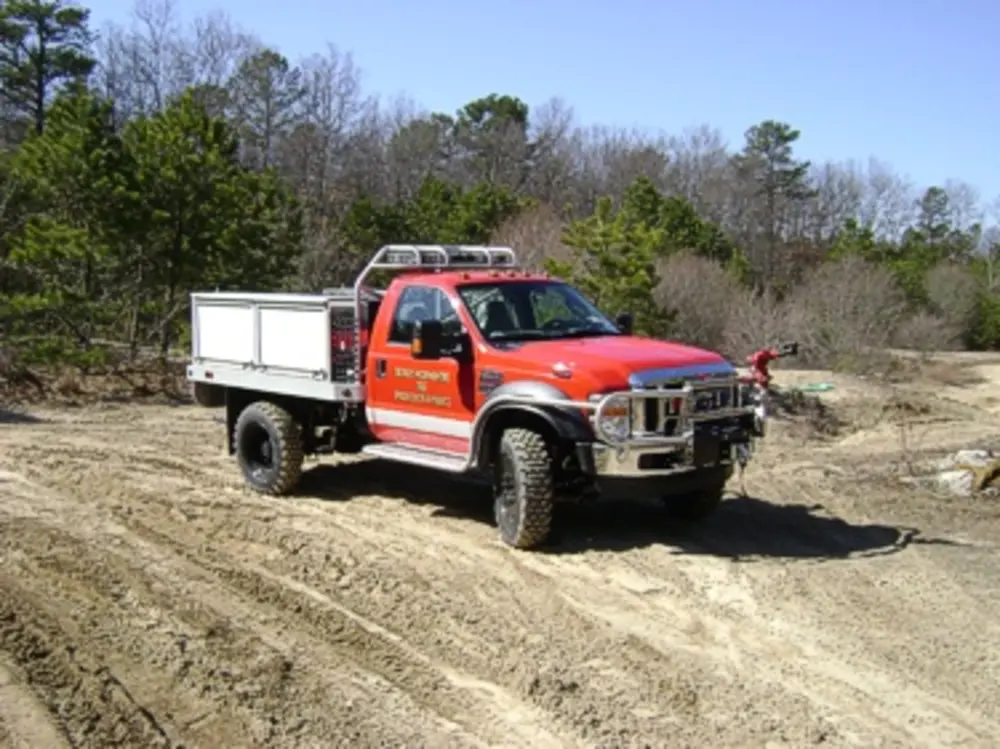 Exterior view of small fire truck showing cab, body compartments, and wheel/tire area.