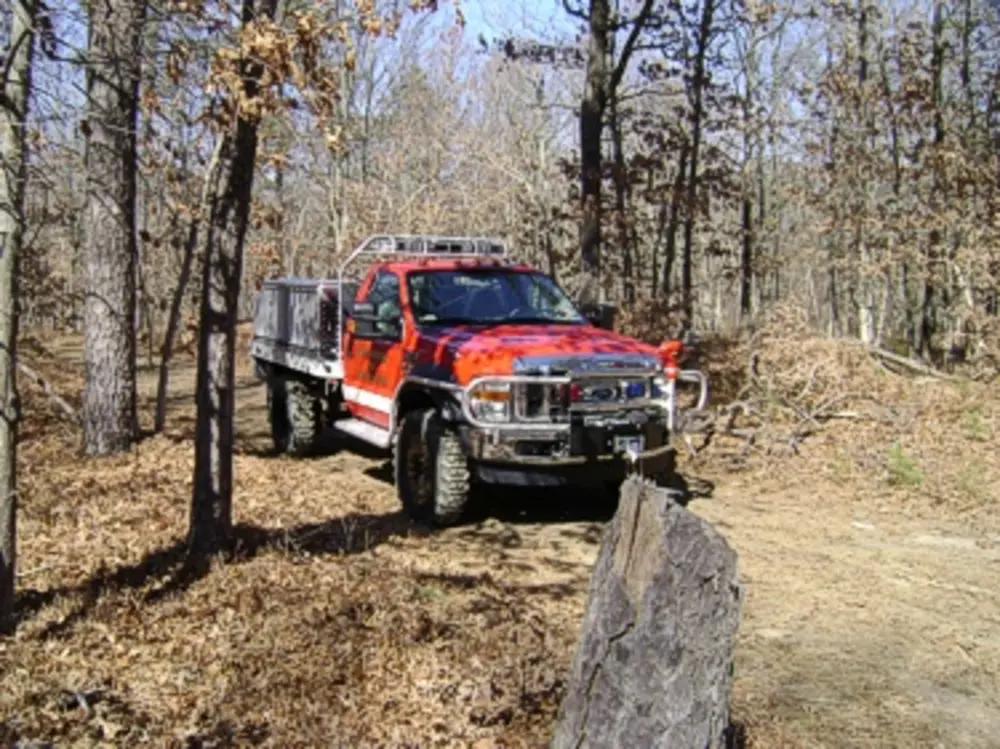Exterior view of small fire truck showing cab, body compartments, and wheel/tire area.