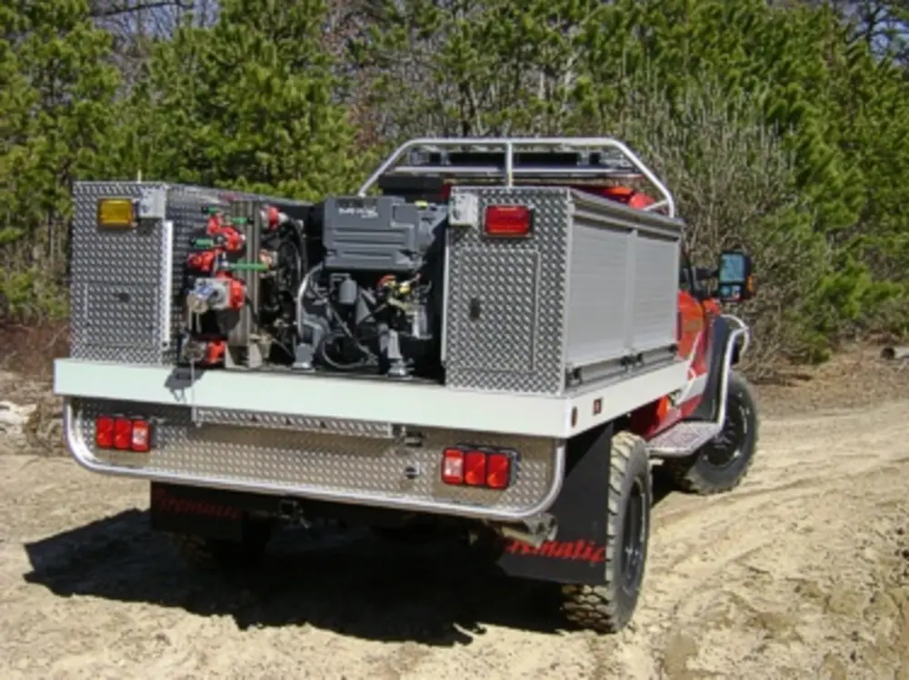 Exterior view of small fire truck showing cab, body compartments, and wheel/tire area.