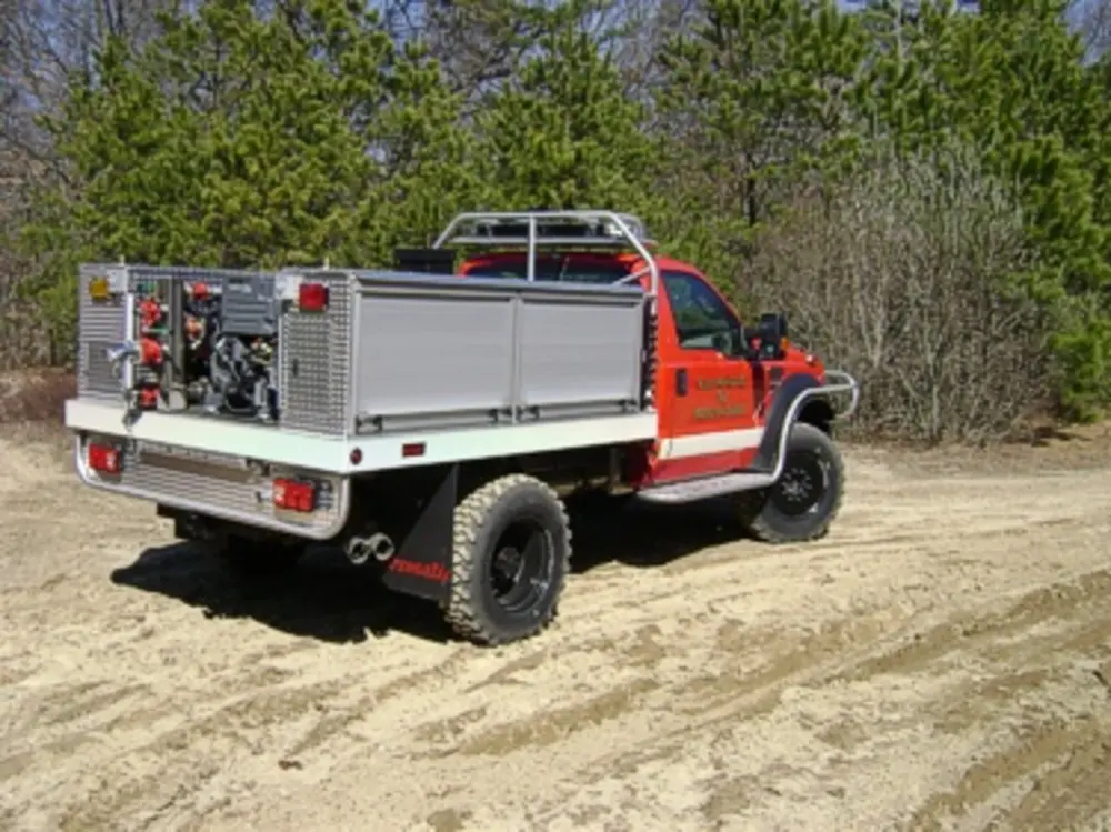 Exterior view of small fire truck showing cab, body compartments, and wheel/tire area.