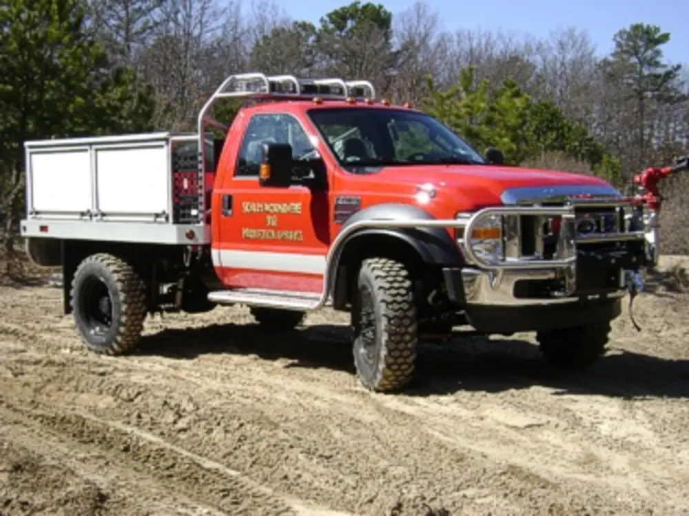 Exterior view of small fire truck showing cab, body compartments, and wheel/tire area.