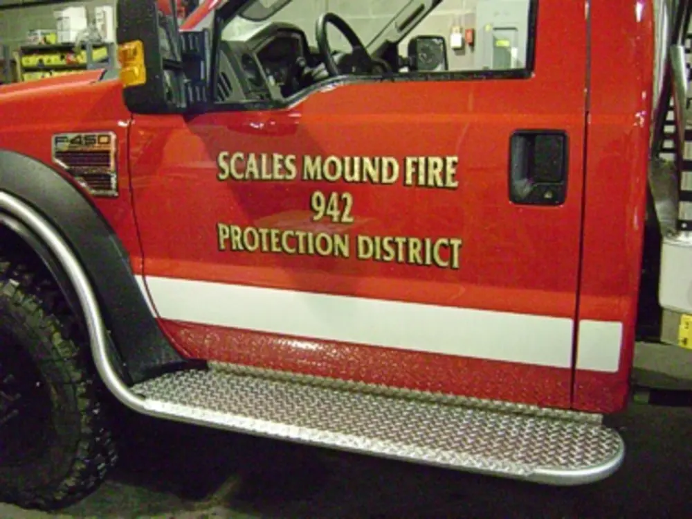 Exterior view of small fire truck showing cab, body compartments, and wheel/tire area.