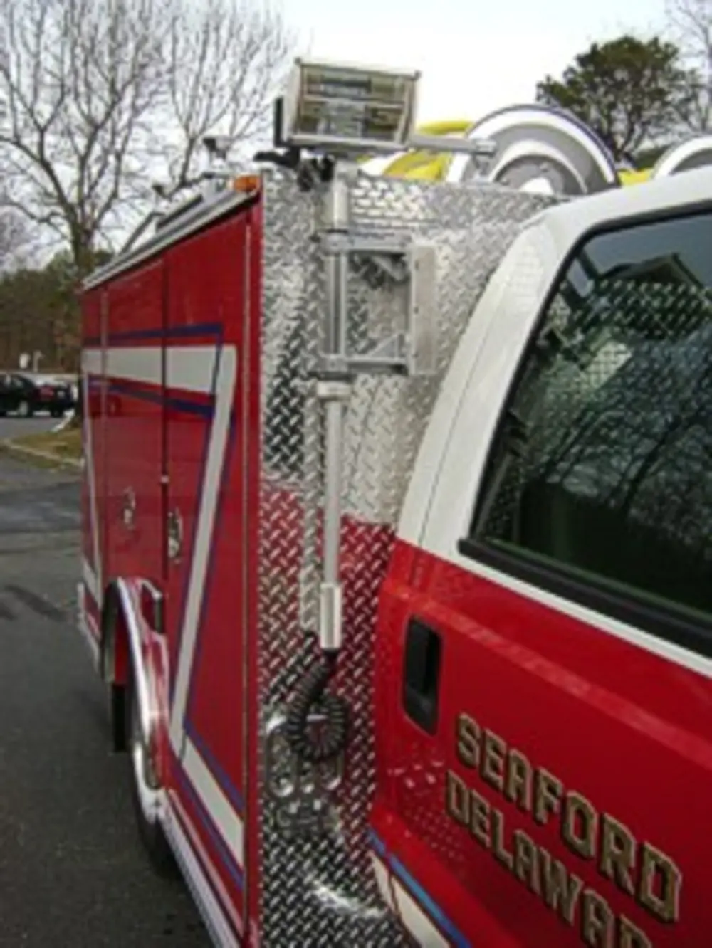 Exterior view of small fire truck showing cab, body compartments, and wheel/tire area.