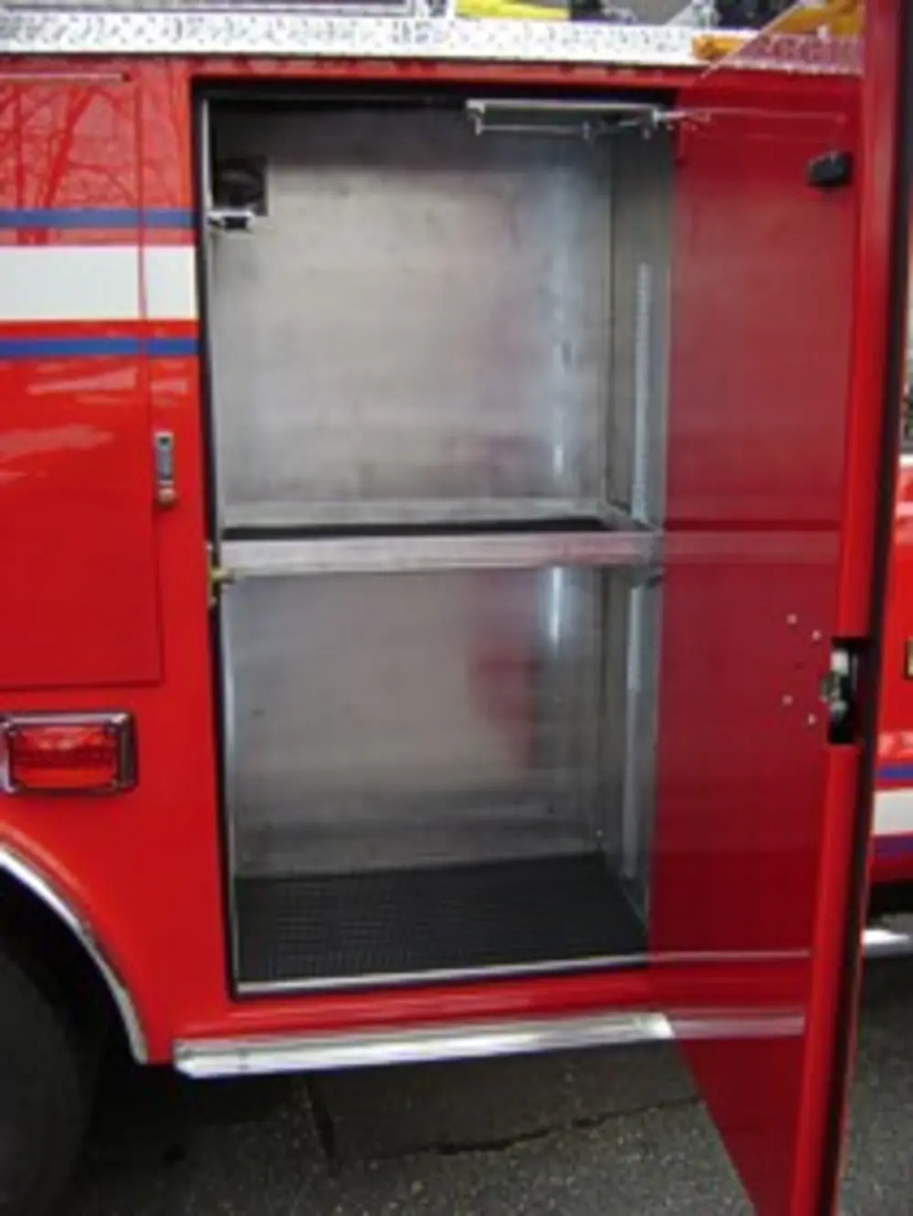 Exterior view of small fire truck showing cab, body compartments, and wheel/tire area.