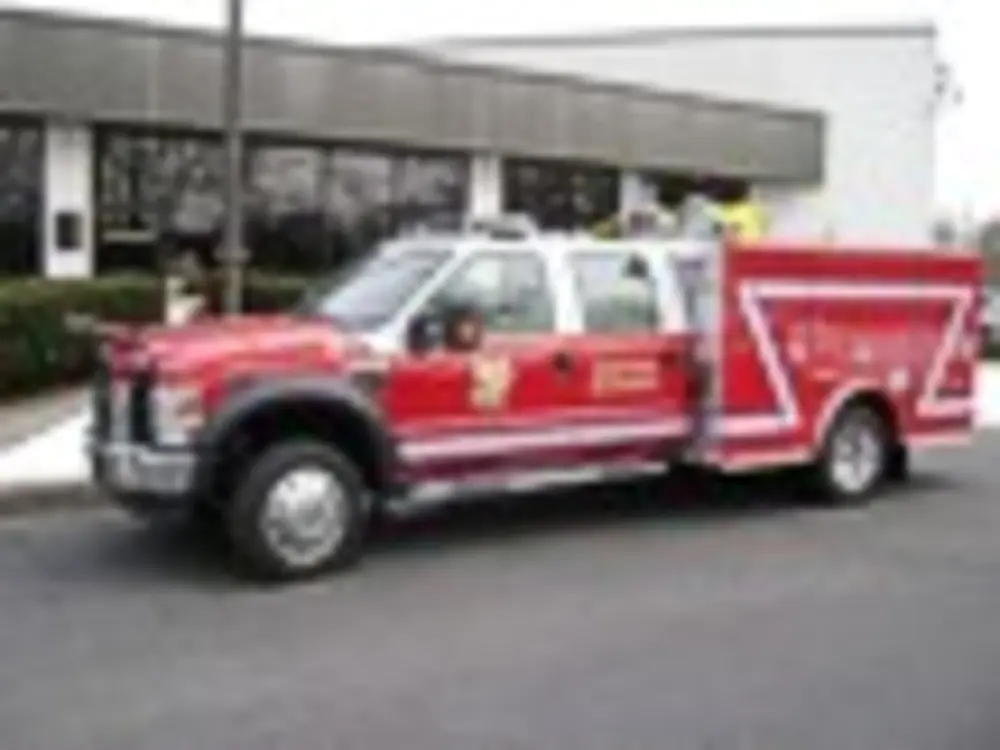 Exterior view of small fire truck showing cab, body compartments, and wheel/tire area.