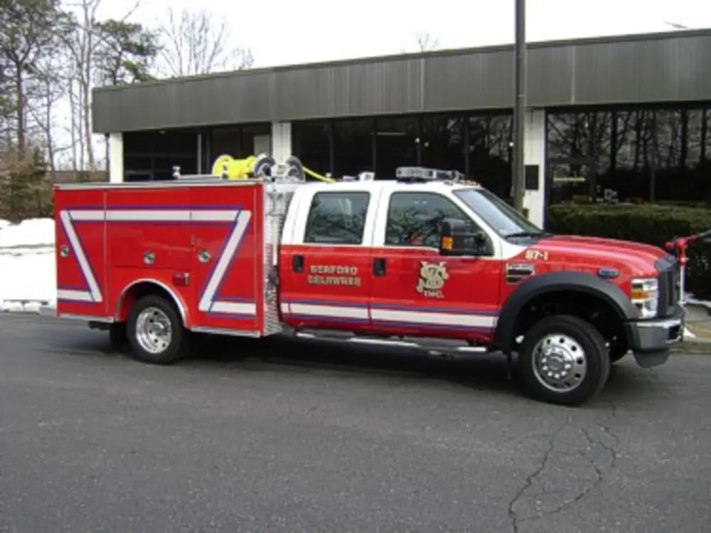 Exterior view of small fire truck showing cab, body compartments, and wheel/tire area.