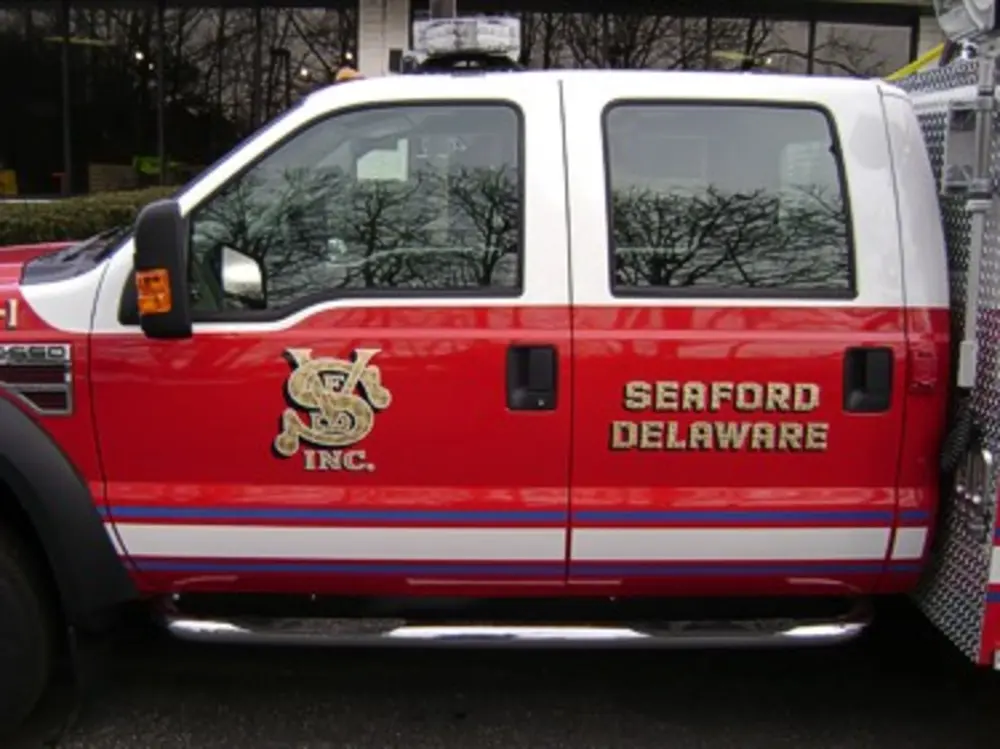 Exterior view of small fire truck showing cab, body compartments, and wheel/tire area.
