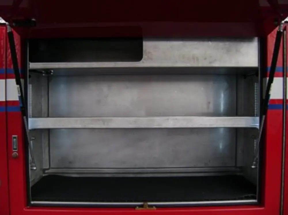 Exterior view of small fire truck showing cab, body compartments, and wheel/tire area.