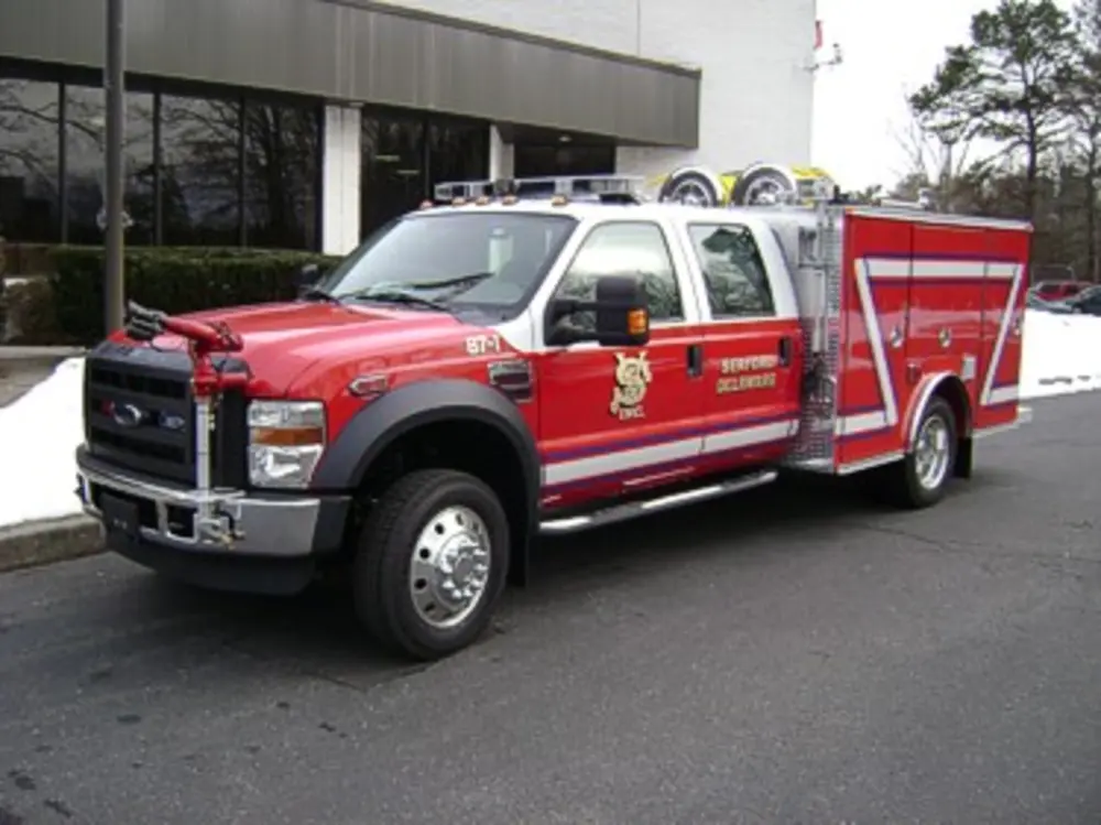 Exterior view of small fire truck showing cab, body compartments, and wheel/tire area.