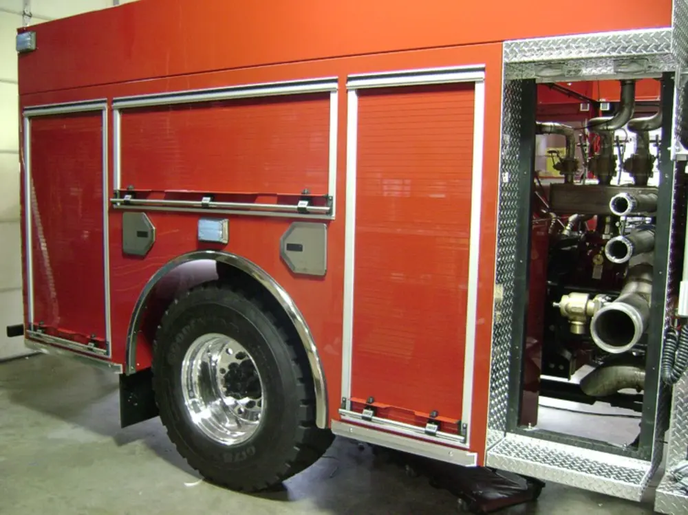 Exterior view of small fire truck showing cab, body compartments, and wheel/tire area.
