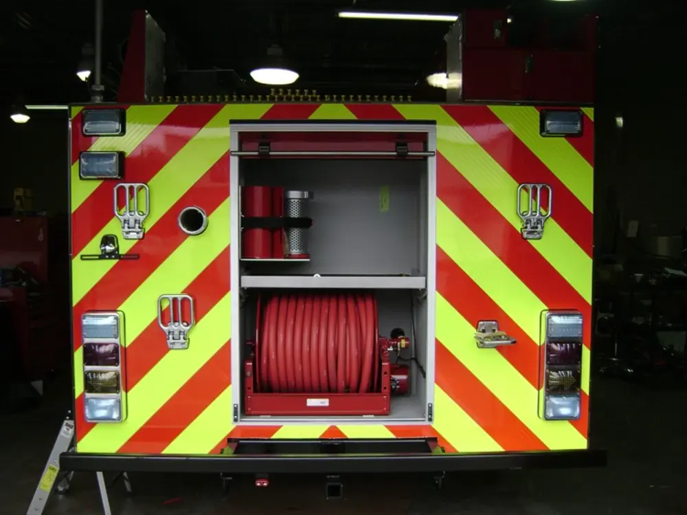 Exterior view of small fire truck showing cab, body compartments, and wheel/tire area.