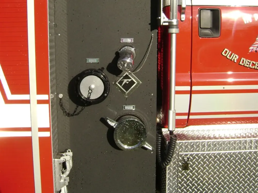Exterior view of small fire truck showing cab, body compartments, and wheel/tire area.