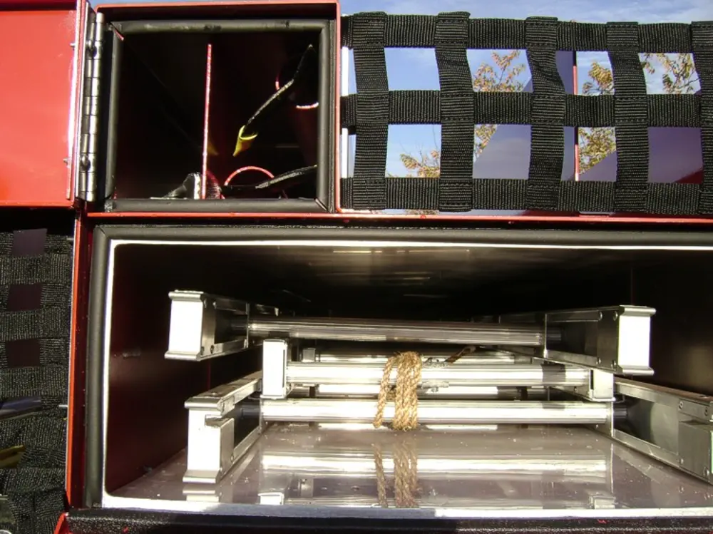 Exterior view of small fire truck showing cab, body compartments, and wheel/tire area.