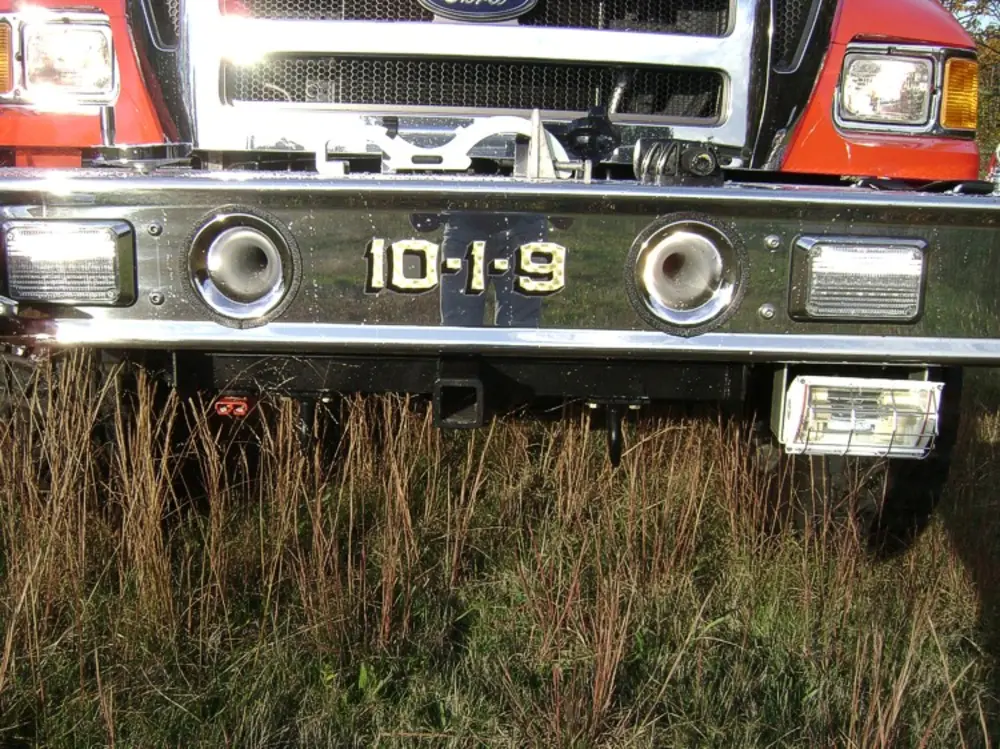 Exterior view of small fire truck showing cab, body compartments, and wheel/tire area.