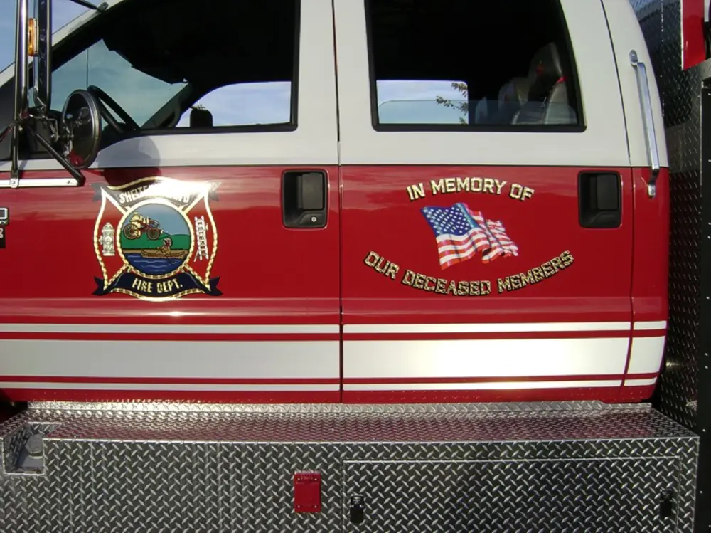 Exterior view of small fire truck showing cab, body compartments, and wheel/tire area.