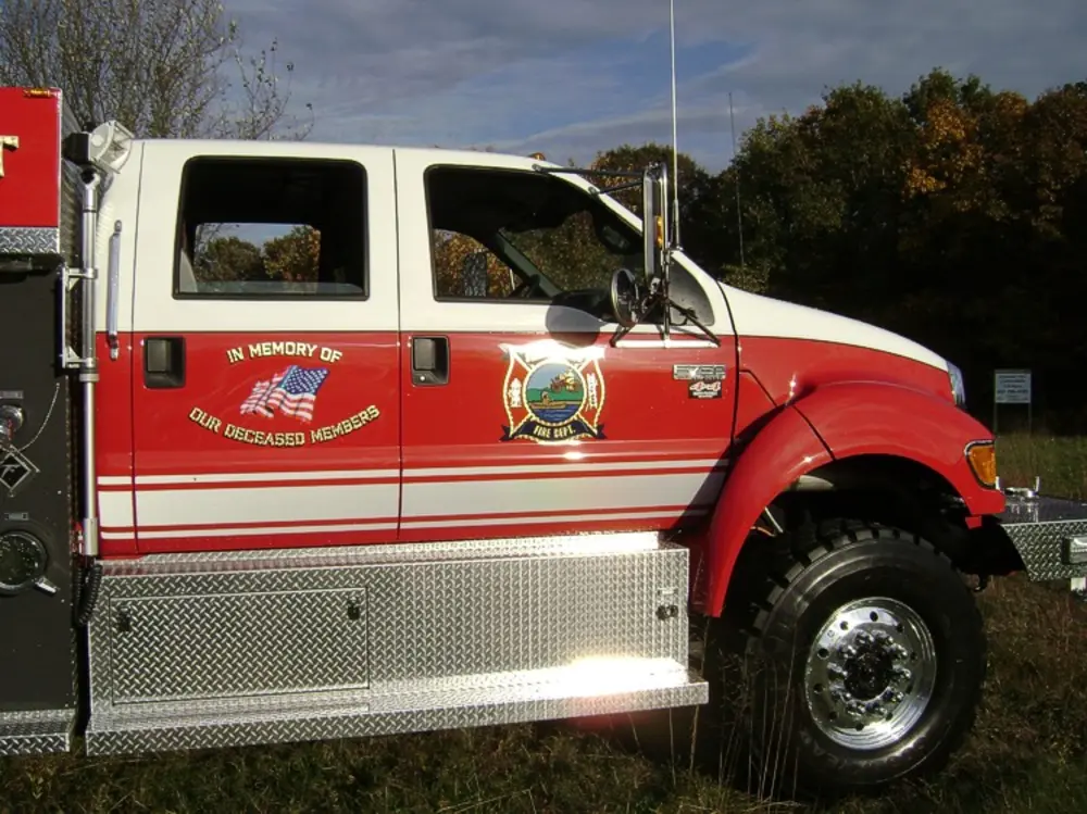 Exterior view of small fire truck showing cab, body compartments, and wheel/tire area.