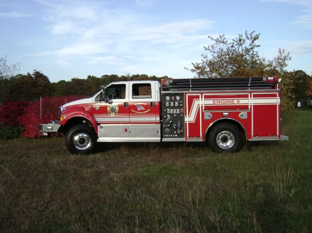 Exterior view of small fire truck showing cab, body compartments, and wheel/tire area.