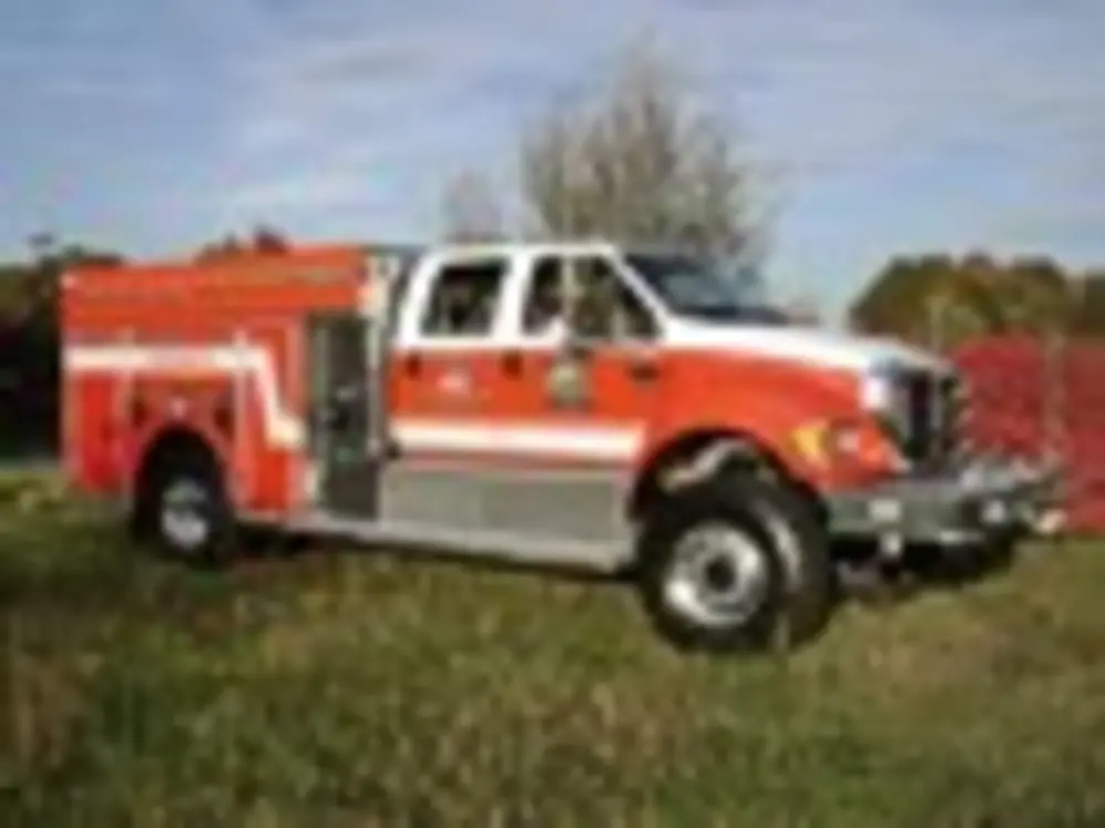 Exterior view of small fire truck showing cab, body compartments, and wheel/tire area.