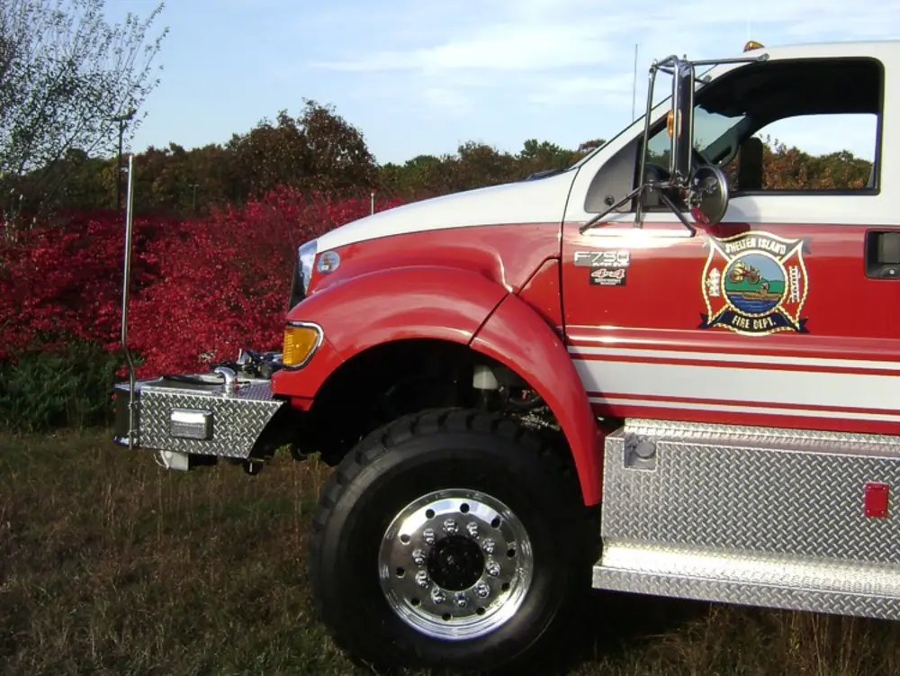 Exterior view of small fire truck showing cab, body compartments, and wheel/tire area.