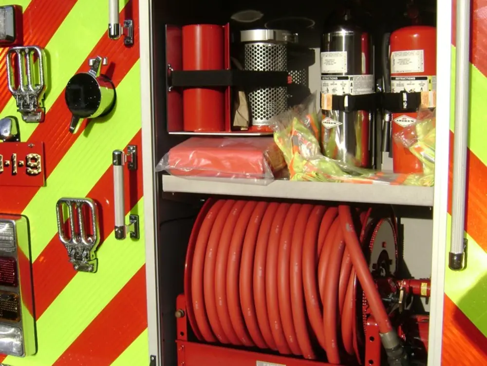 Exterior view of small fire truck showing cab, body compartments, and wheel/tire area.