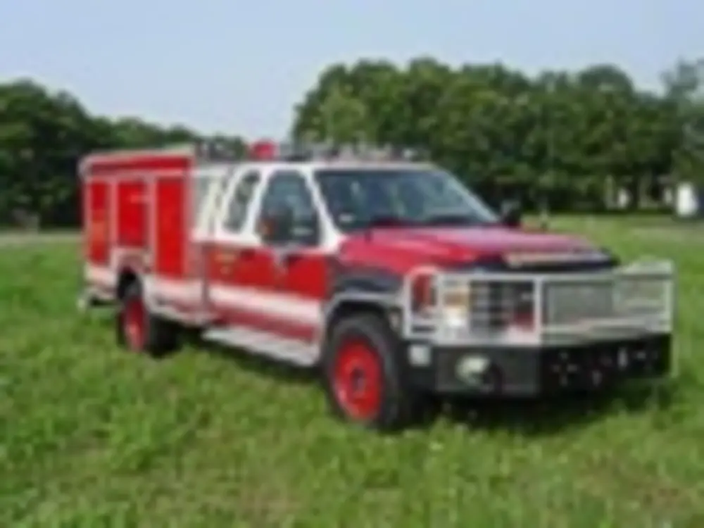 Exterior view of small fire truck showing cab, body compartments, and wheel/tire area.