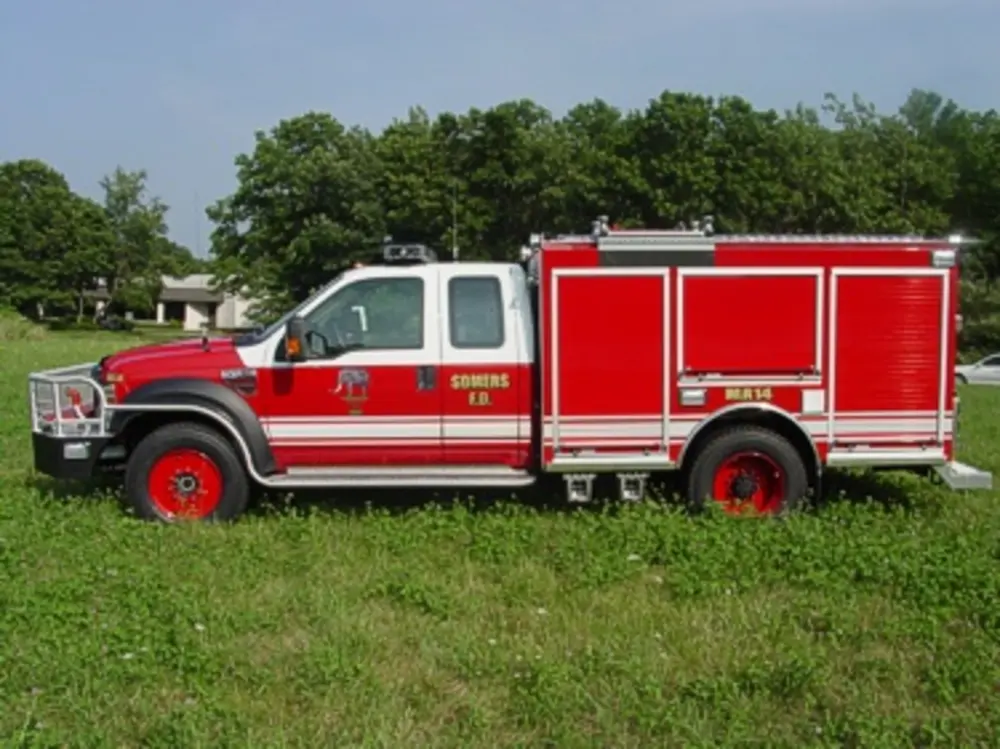 Exterior view of small fire truck showing cab, body compartments, and wheel/tire area.